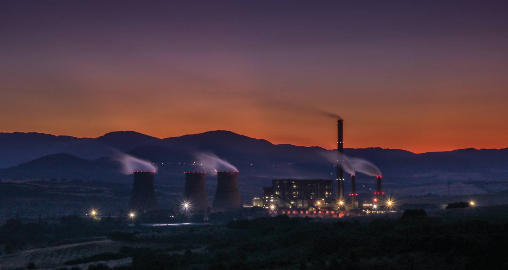 A gold refinery complex at dusk with cooling towers and glowing lights